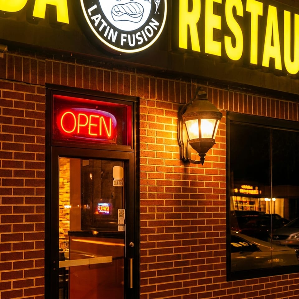 Brightly lit brick Latin Fusion restaurant exterior at night with an 'OPEN' sign and glowing lantern.