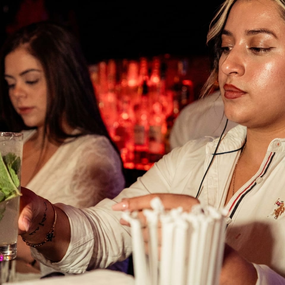 Bartender in white shirt holding a mojito with mint and lemon at a bar.