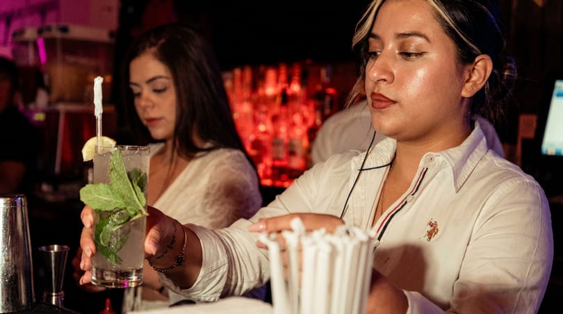 Bartender in white shirt holding a mojito with mint and lemon at a bar.