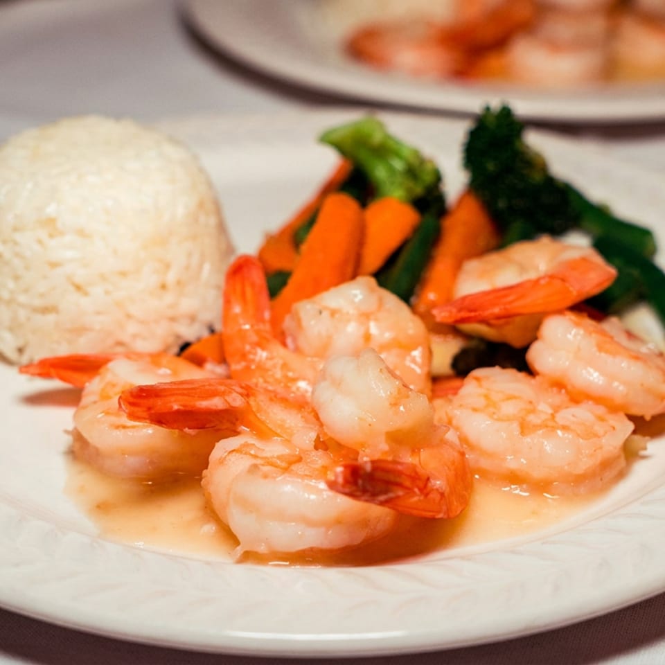 Shrimp, white rice, and colorful steamed vegetables served on a white plate.